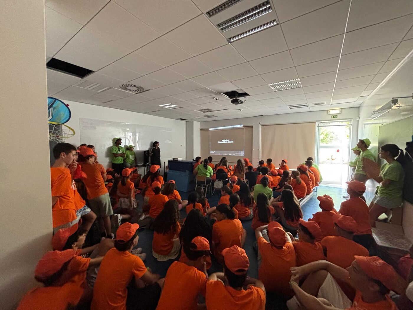 Grupo de participantes de t-shirt laranja numa actividade em sala