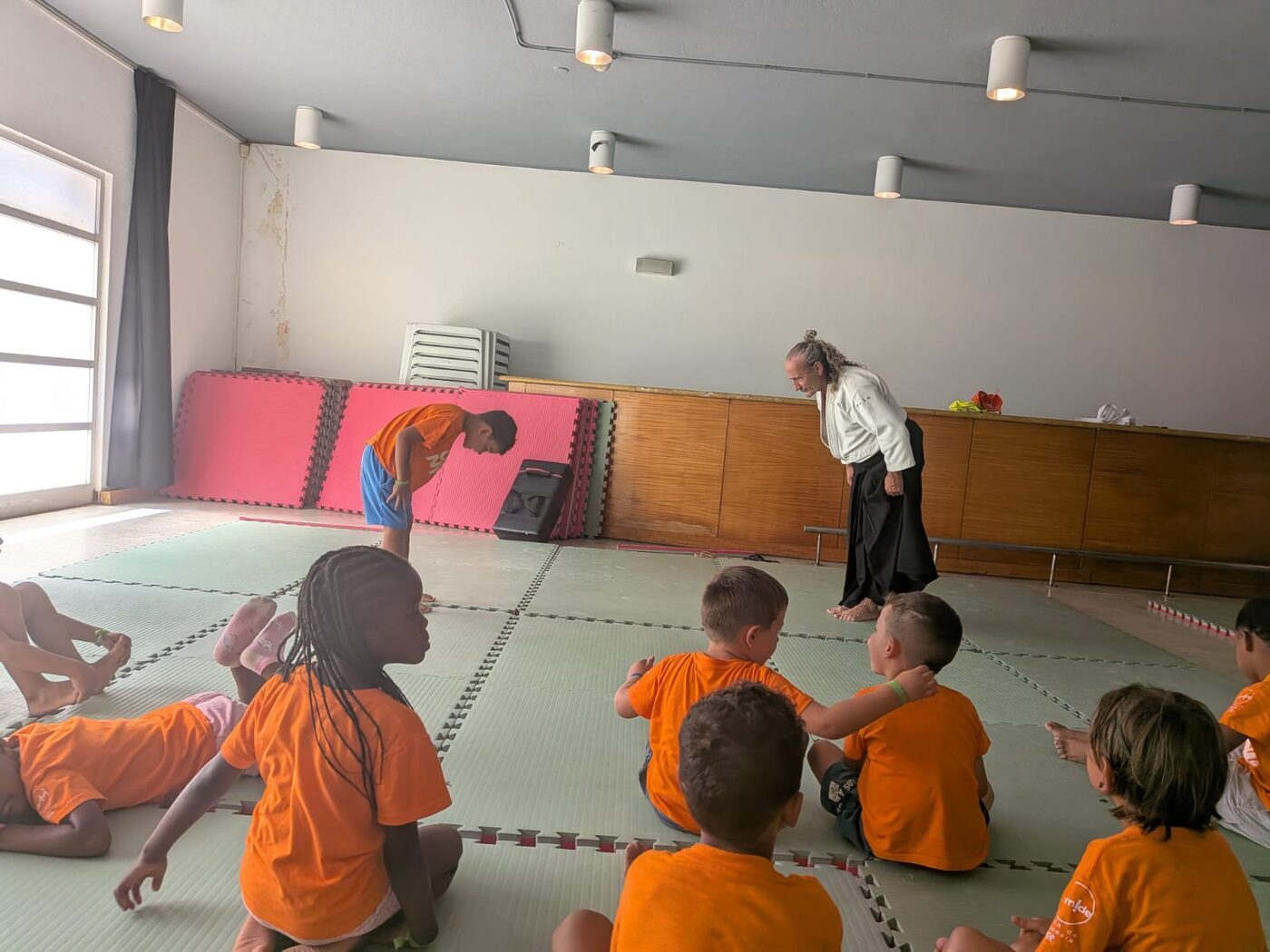 Aula num ginásio, com crianças sentadas em frente à monitora