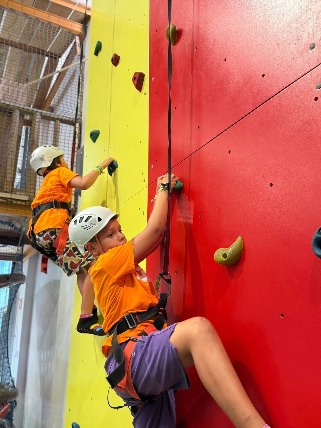 Criança de capacete a subir uma parede de escalada vermelha e amarela