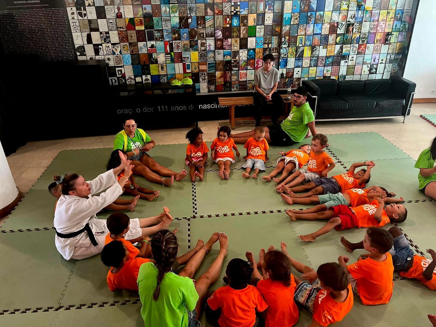 Grupo de crianças sentado em roda num tapete de dojo, numa aula de artes marciais