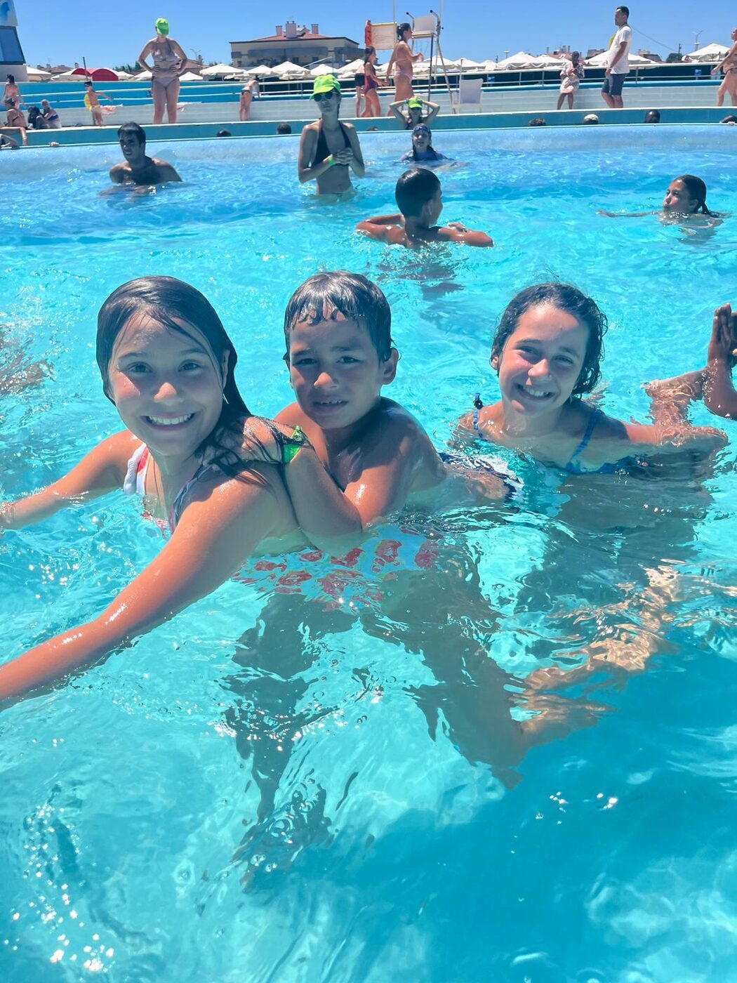 Monitora e duas crianças a sorrir dentro da piscina