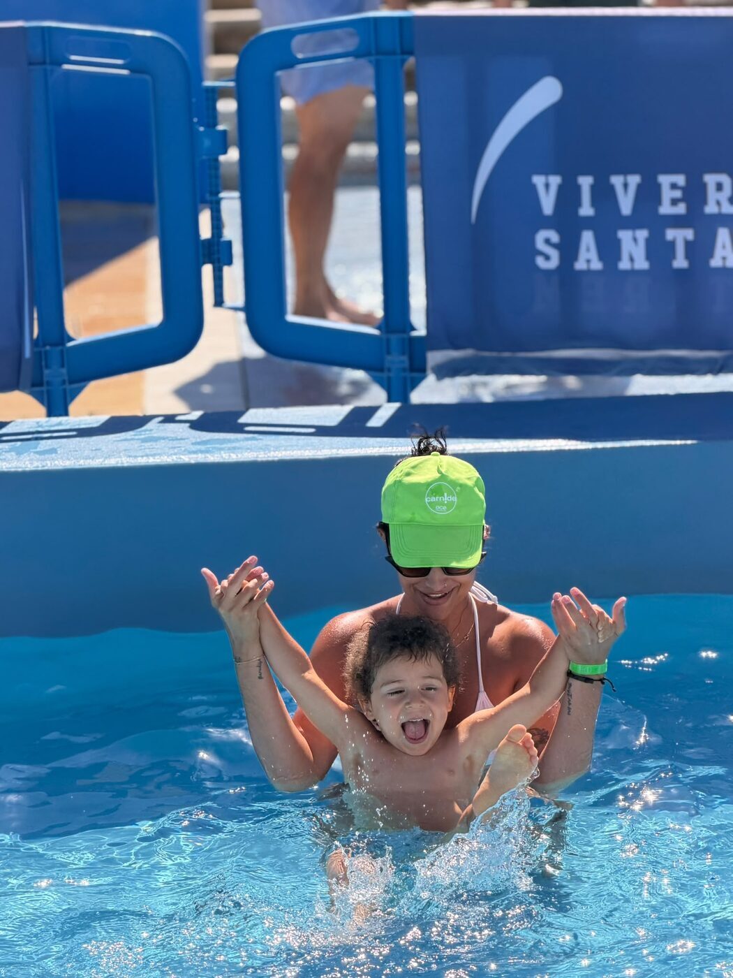 Criança a rir ao colo de uma monitora dentro da piscina