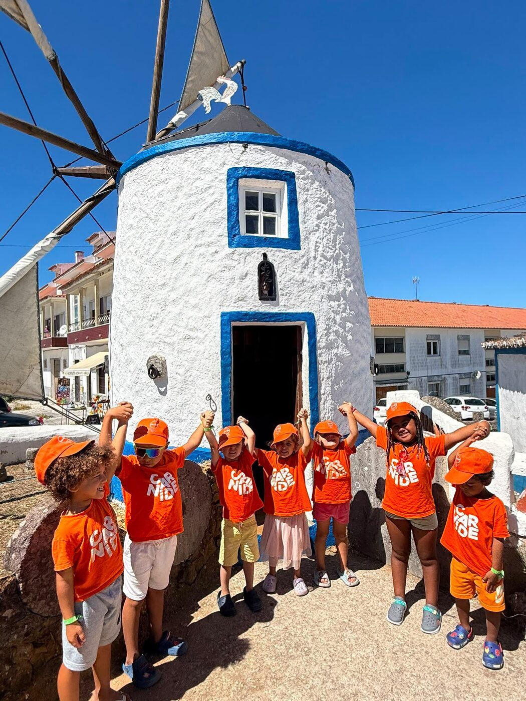 Grupo de crianças à porta de um moinho de vento caiado de branco e azul