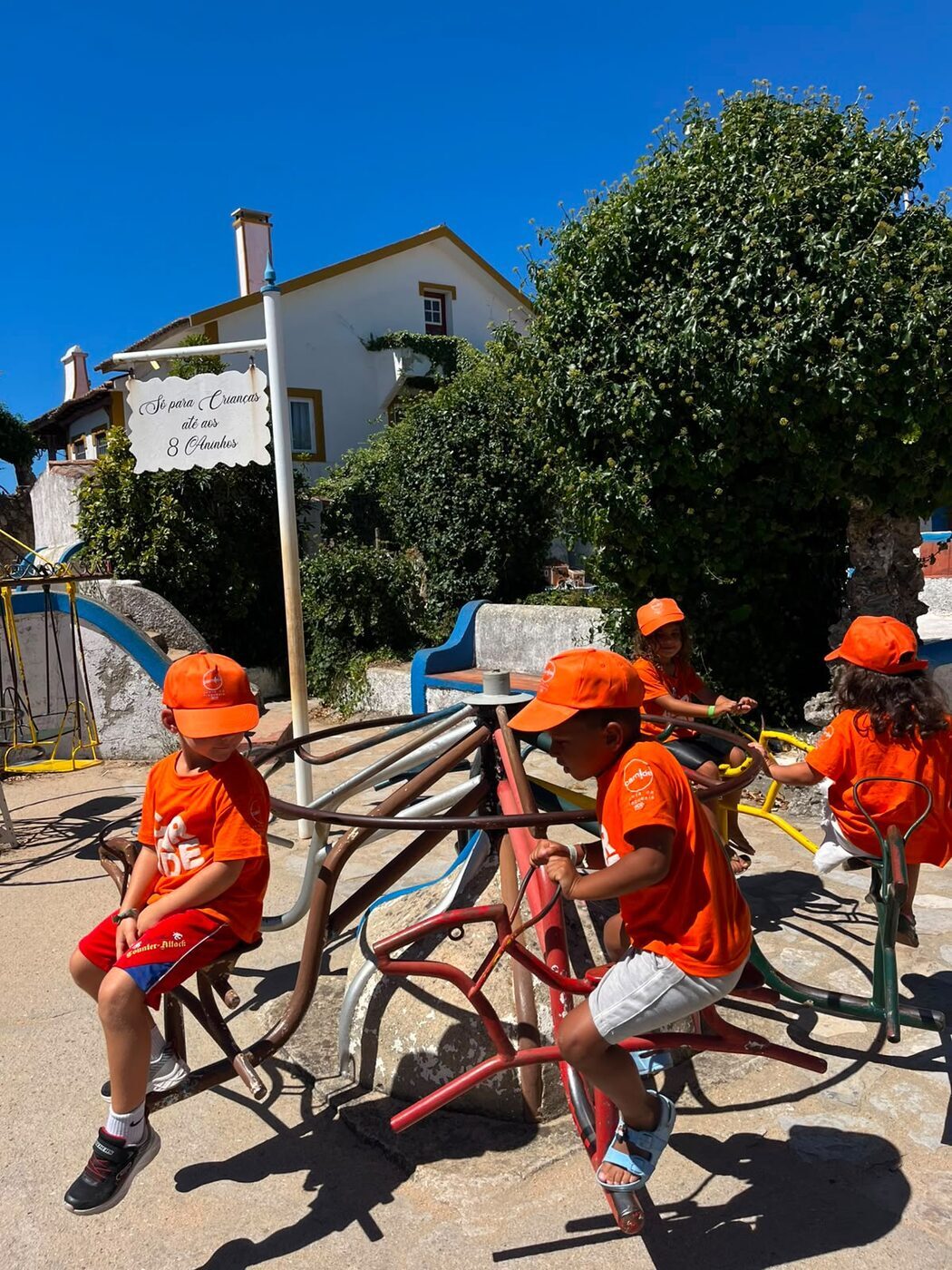 Crianças a pedalar em bicicletas fixas num recreio ao ar livre