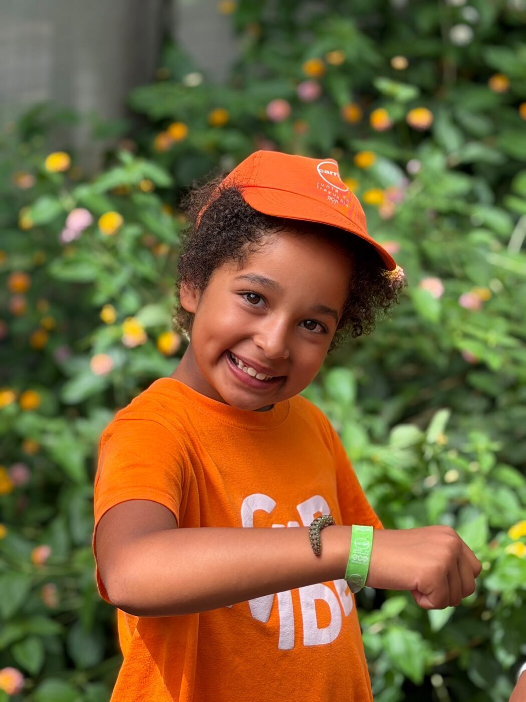 Menina de boné laranja a sorrir num jardim florido