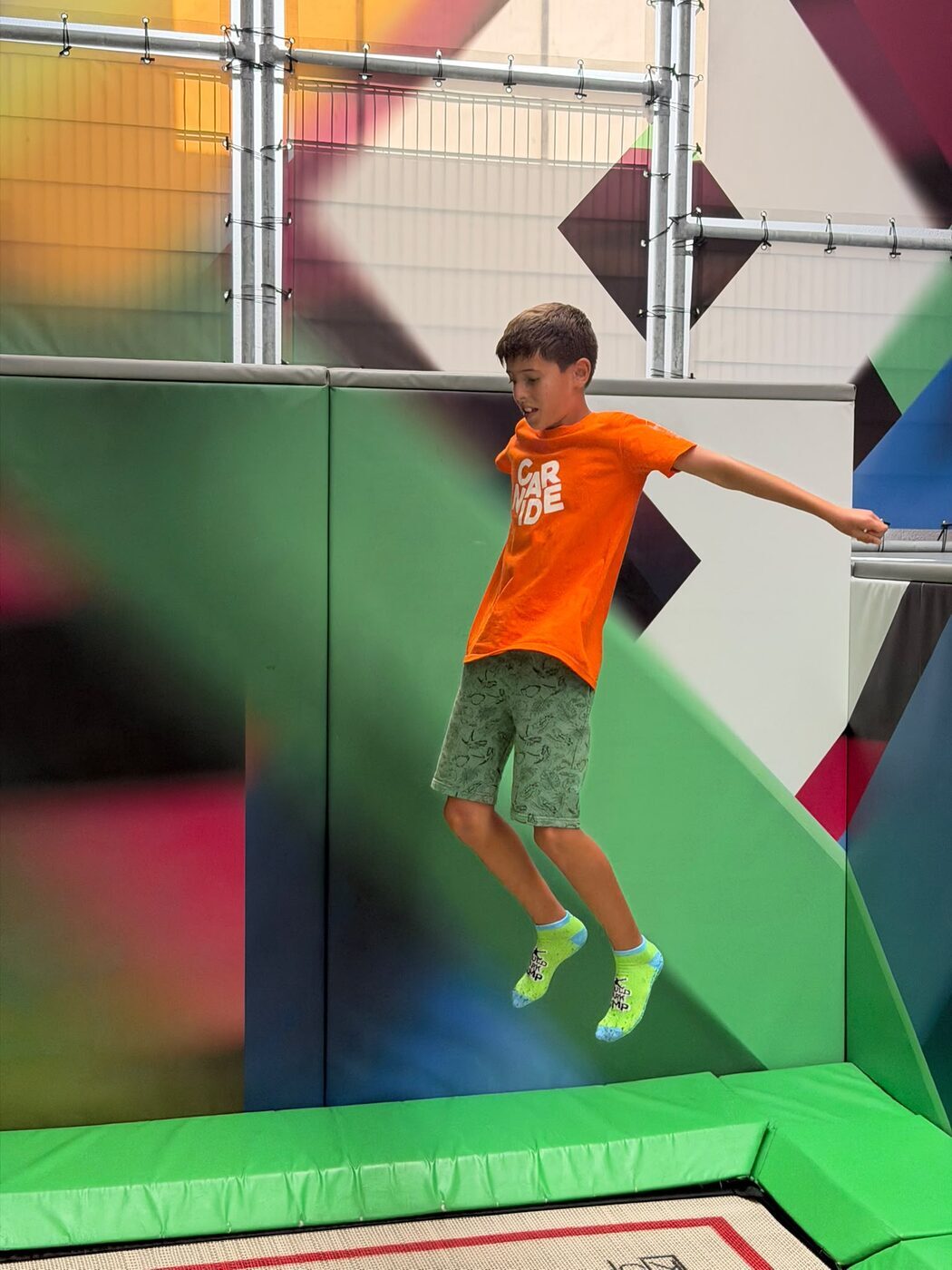 Menino a saltar num trampolim, diante de uma parede de padrões coloridos