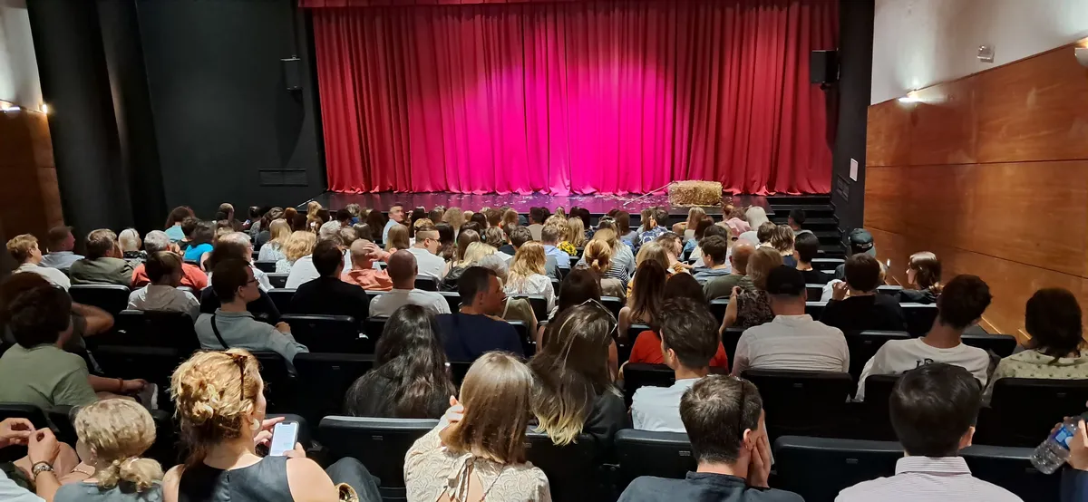 Plateia cheia no auditório, com a cortina do palco ao fundo