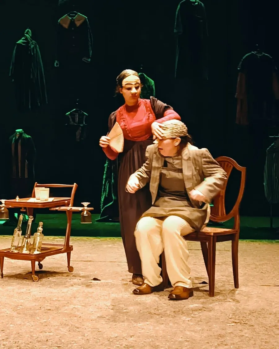 Dois actores em cena numa peça de teatro, com cenário de época